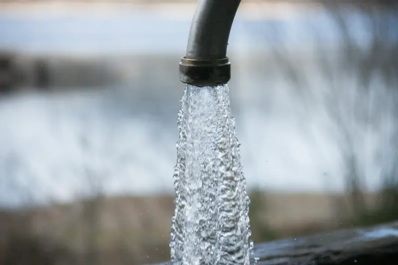 Outdoor water spigot on a rural property with a grassy hillside behind it